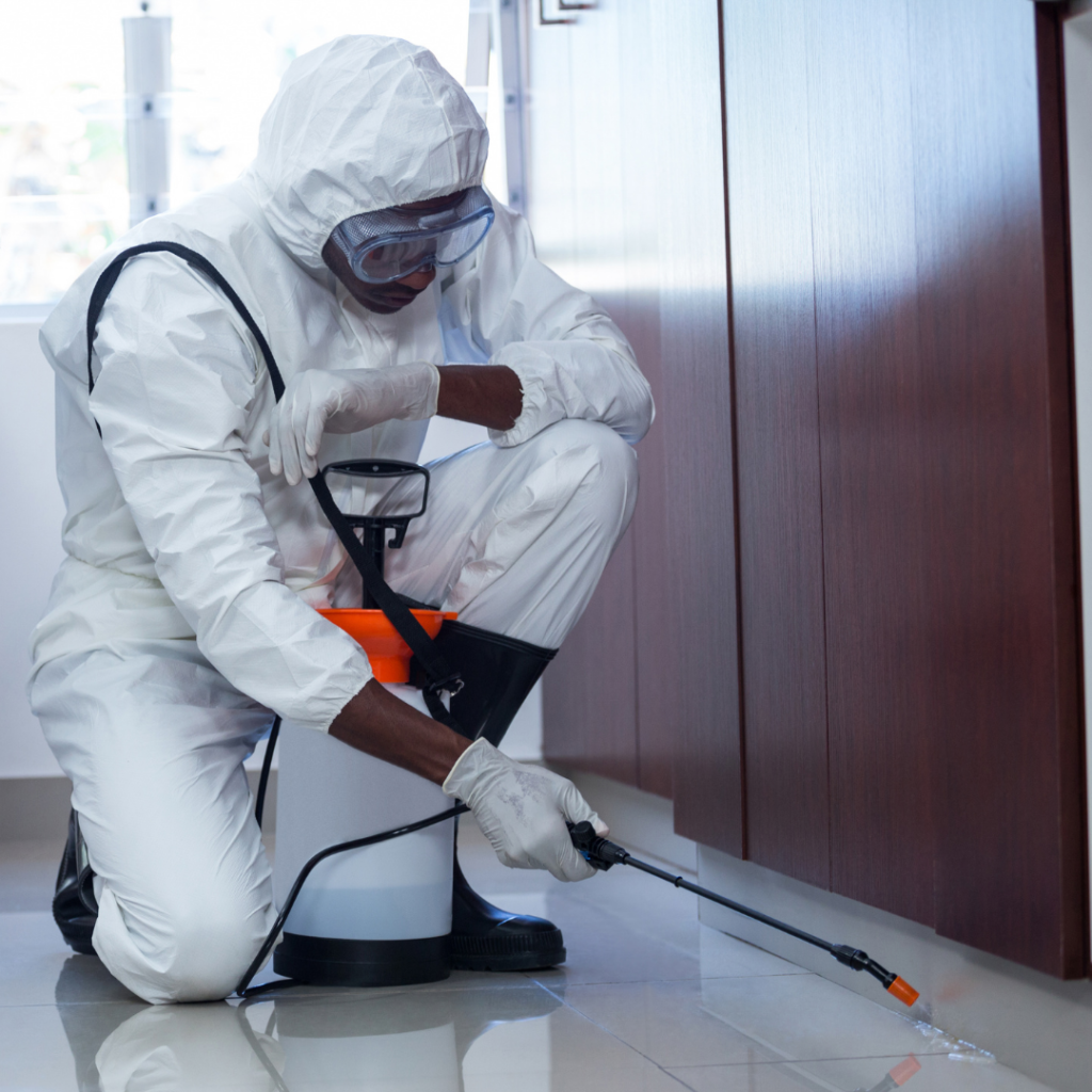 African american male in white pest control outfit spraying around the edges of a cabinet